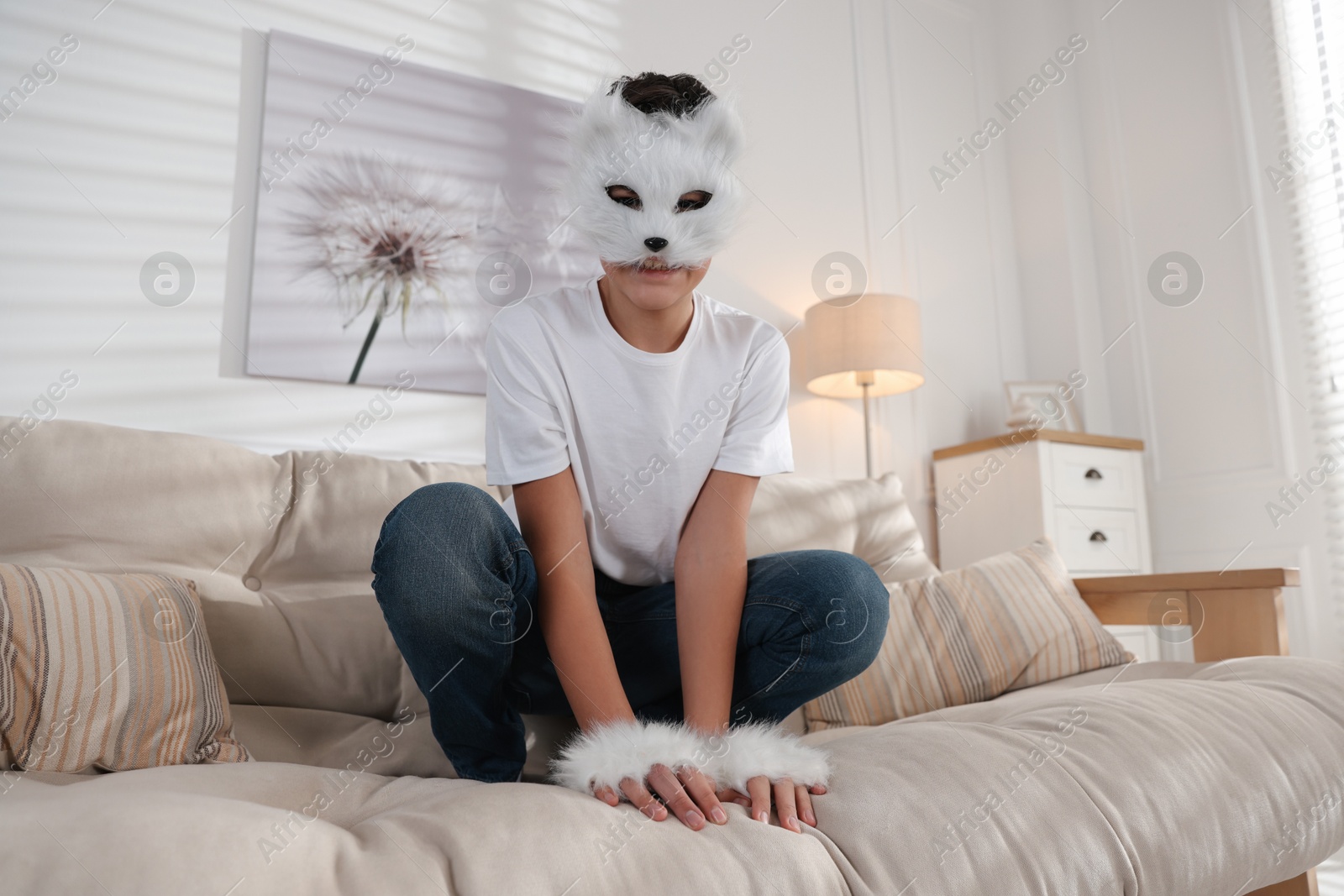 Photo of Quadrobics. Boy wearing cat mask and gloves on sofa at home