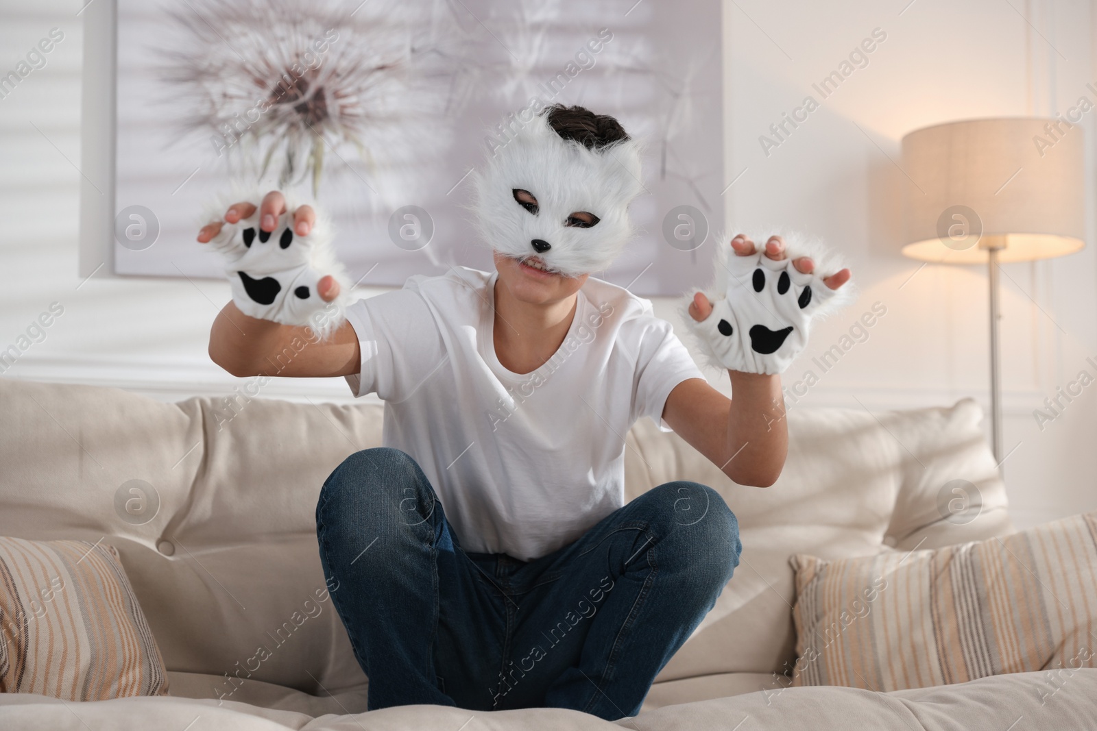 Photo of Quadrobics. Boy wearing cat mask and gloves on sofa at home