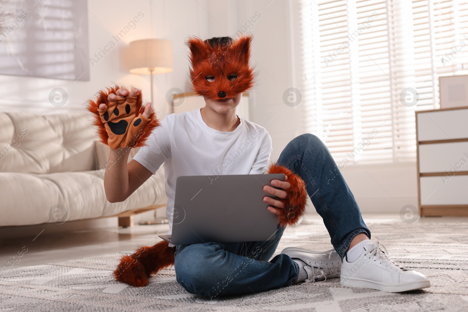 Photo of Quadrobics. Boy in fox mask, gloves and tail holding laptop at home