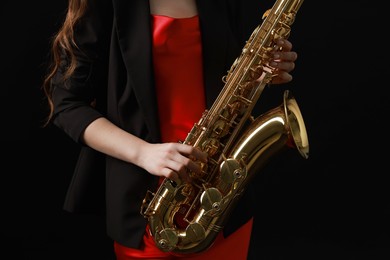 Photo of Professional musician with saxophone on black background, closeup