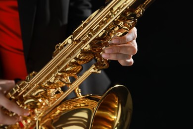 Photo of Professional musician with saxophone on black background, closeup