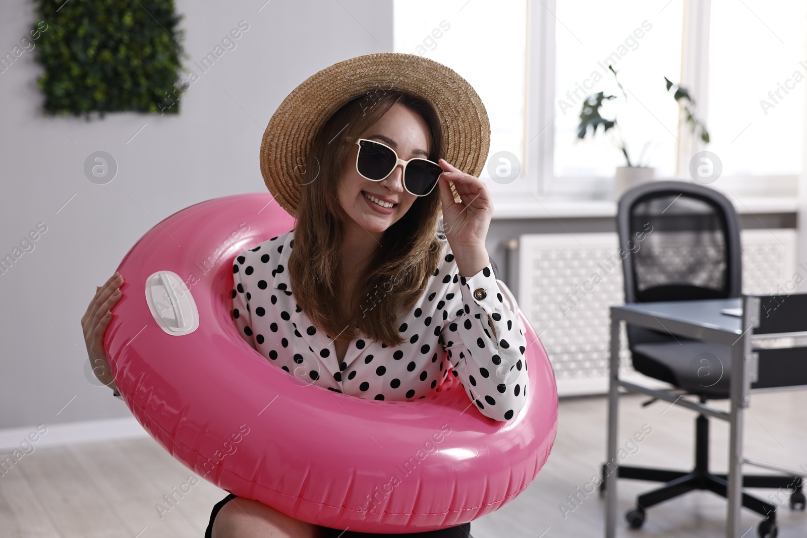 Photo of Businesswoman with inflatable ring, straw hat and sunglasses in office