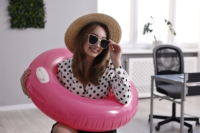 Photo of Businesswoman with inflatable ring, straw hat and sunglasses in office