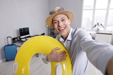 Photo of Businessman with inflatable ring, straw hat and sunglasses taking selfie in office