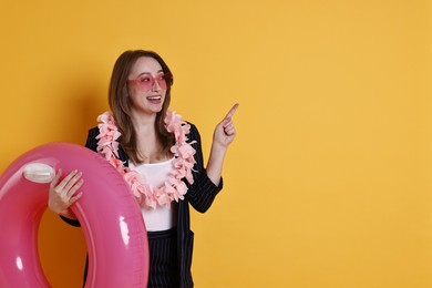 Photo of Businesswoman with inflatable ring, flower wreath and sunglasses pointing on orange background, space for text