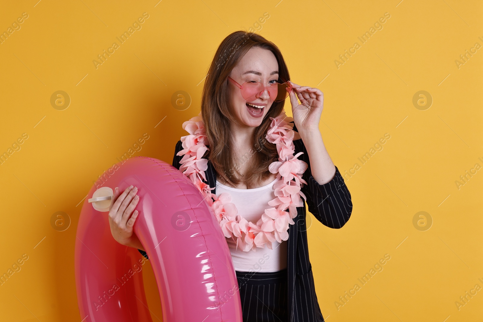 Photo of Businesswoman with inflatable ring, flower wreath and sunglasses on orange background