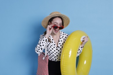 Photo of Businesswoman with inflatable ring, straw hat, bag and sunglasses on light blue background