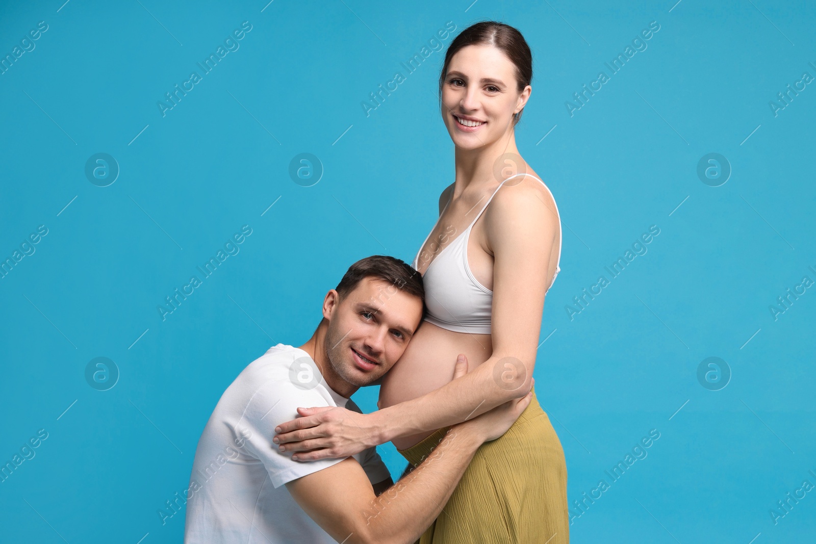 Photo of Man listening to baby in his pregnant wife's belly on blue background