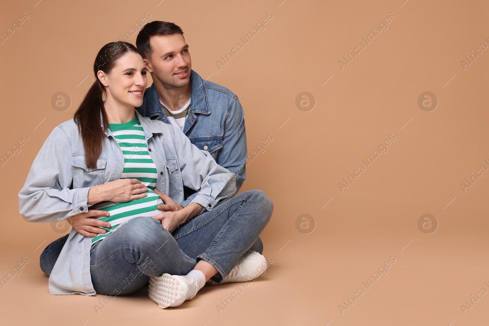 Photo of Pregnant woman and her husband on beige background. Space for text