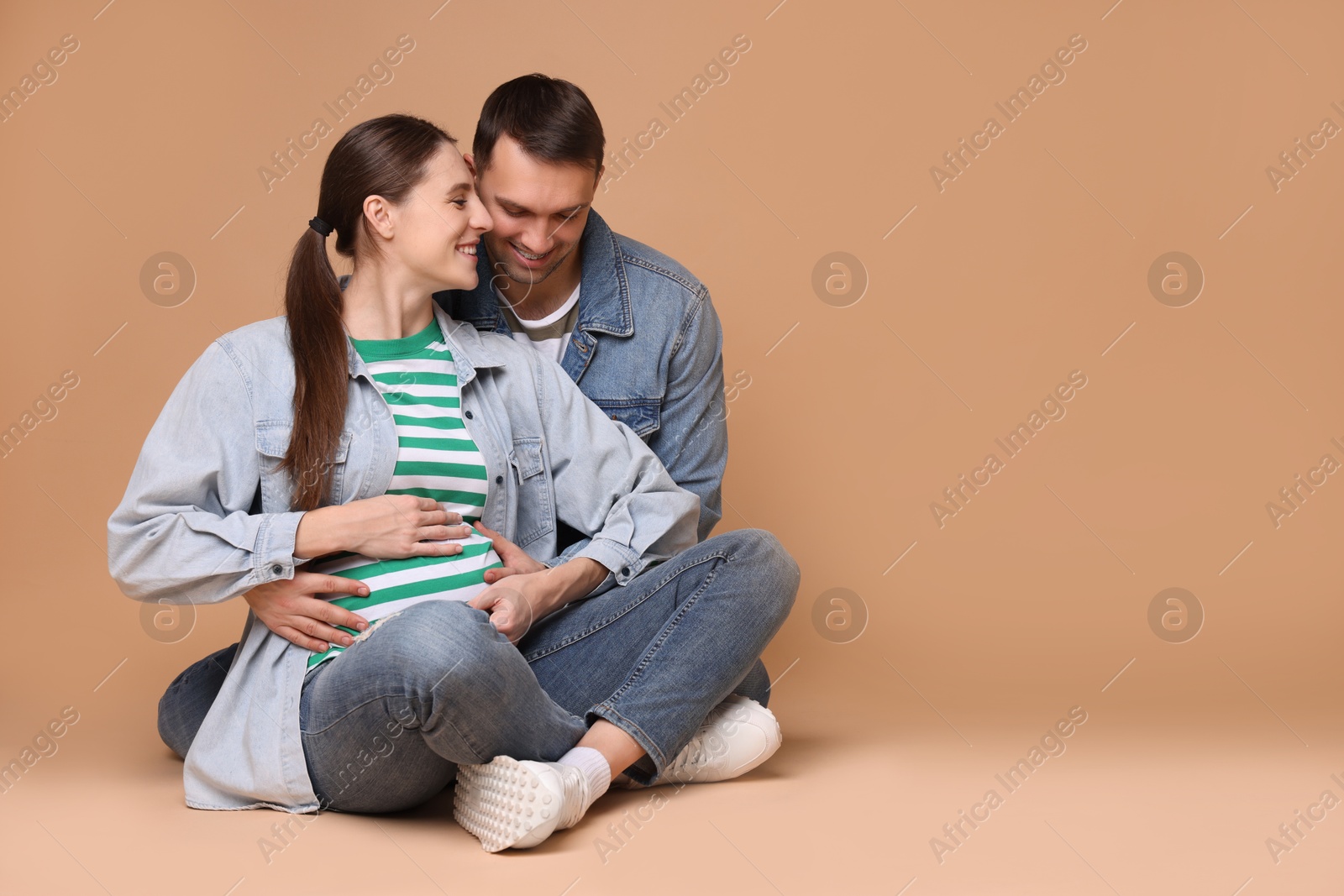 Photo of Pregnant woman and her husband on beige background. Space for text