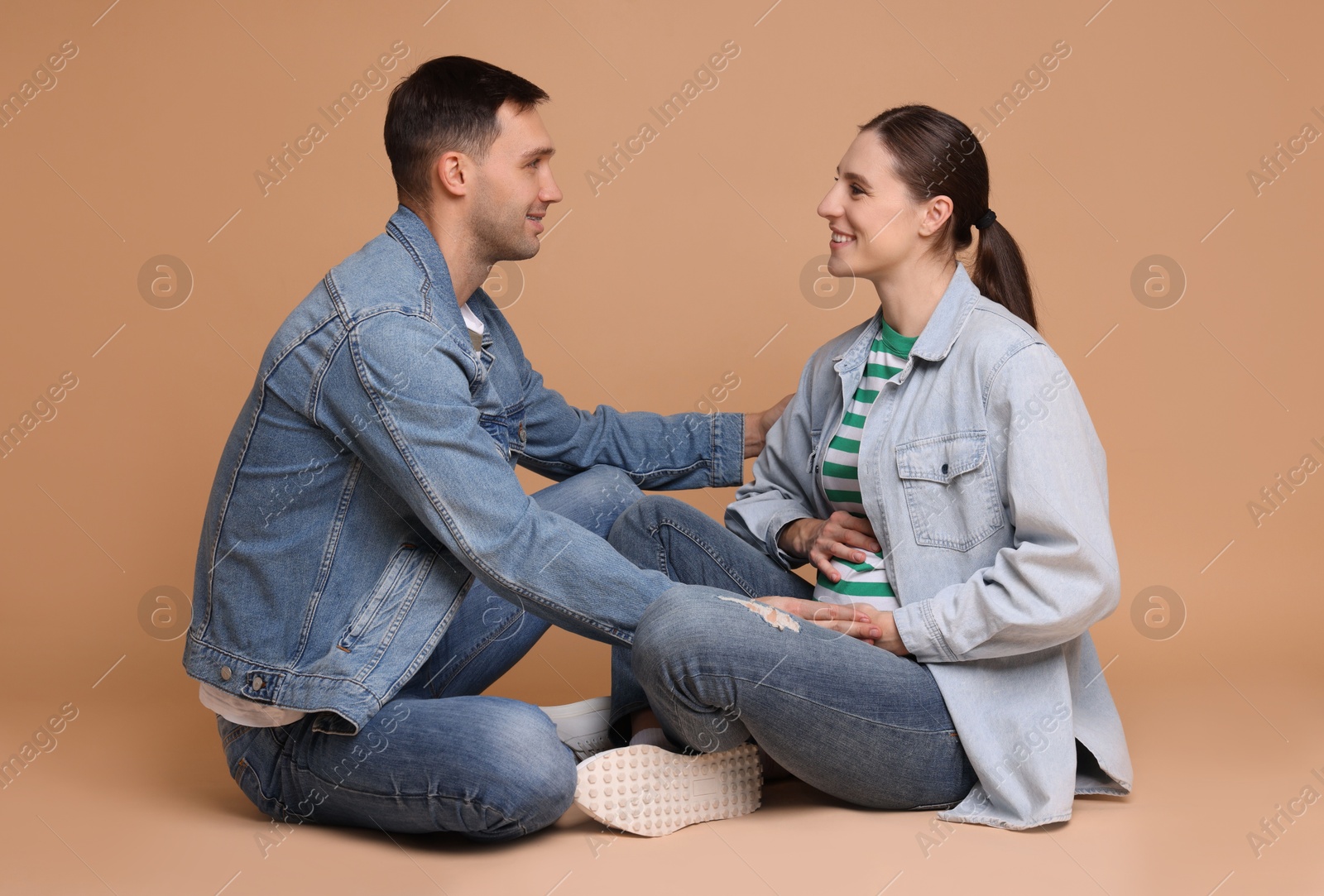 Photo of Man trying to feel baby kicks in his pregnant wife's belly on beige background