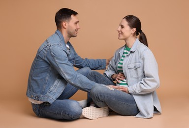 Photo of Man trying to feel baby kicks in his pregnant wife's belly on beige background