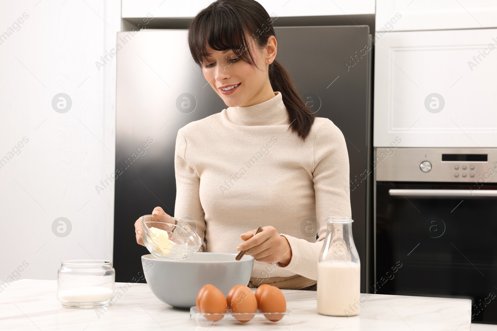 Photo of Making dough. Woman adding butter into bowl at white marble table