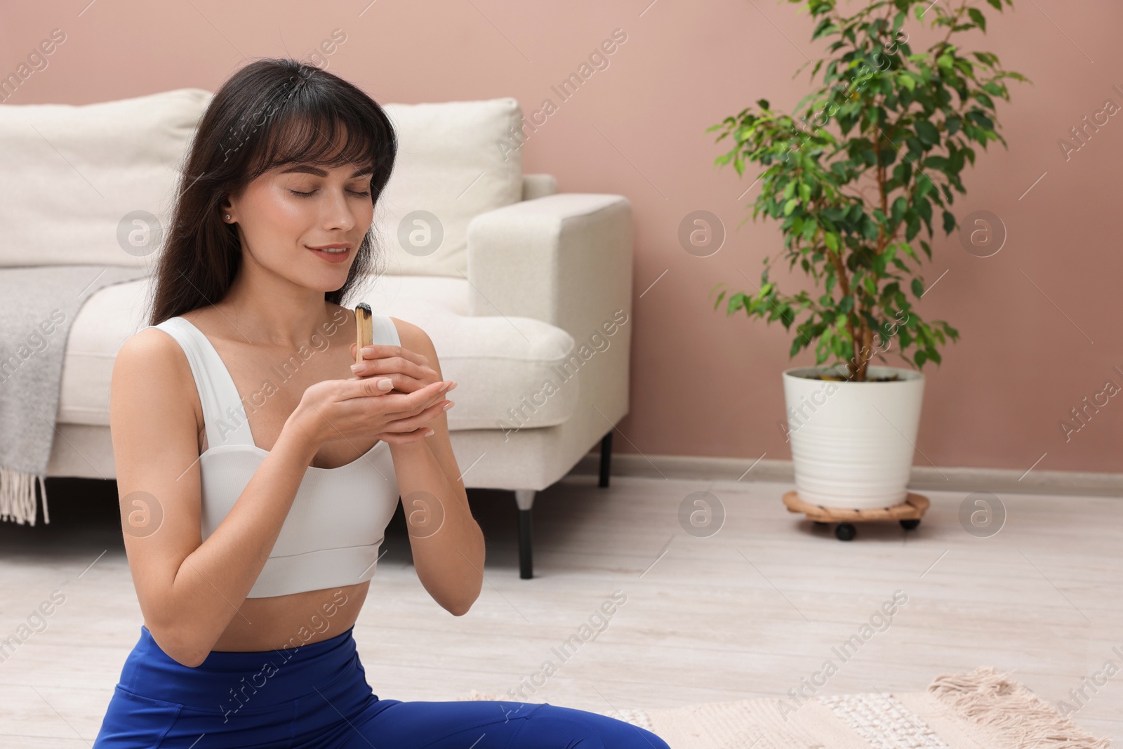 Photo of Woman with smoldering palo santo stick on floor at home, space for text