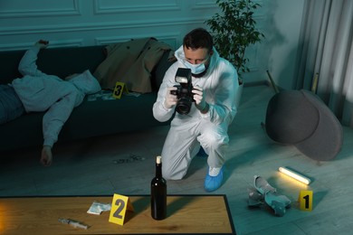 Photo of Forensic expert with camera working at crime scene and dead woman's body indoors