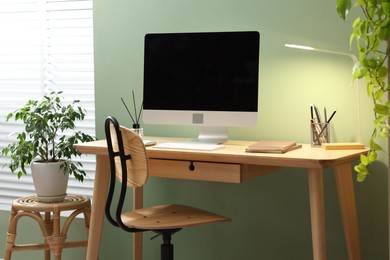 Photo of Home office. Comfortable workplace near light green wall. Desk with computer and other furniture in room