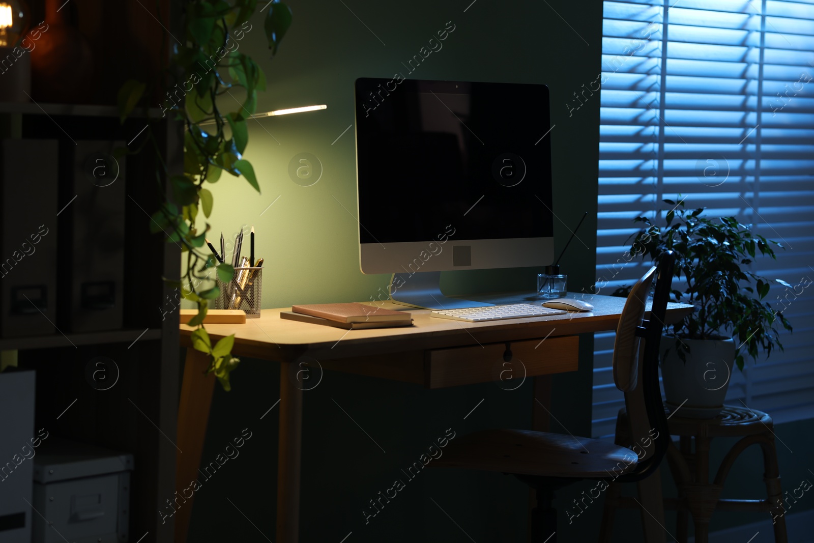 Comfortable workplace with computer and lamp on wooden desk at home office in evening Photo of Comfortable workplace with computer and lamp on wooden desk at home office in evening