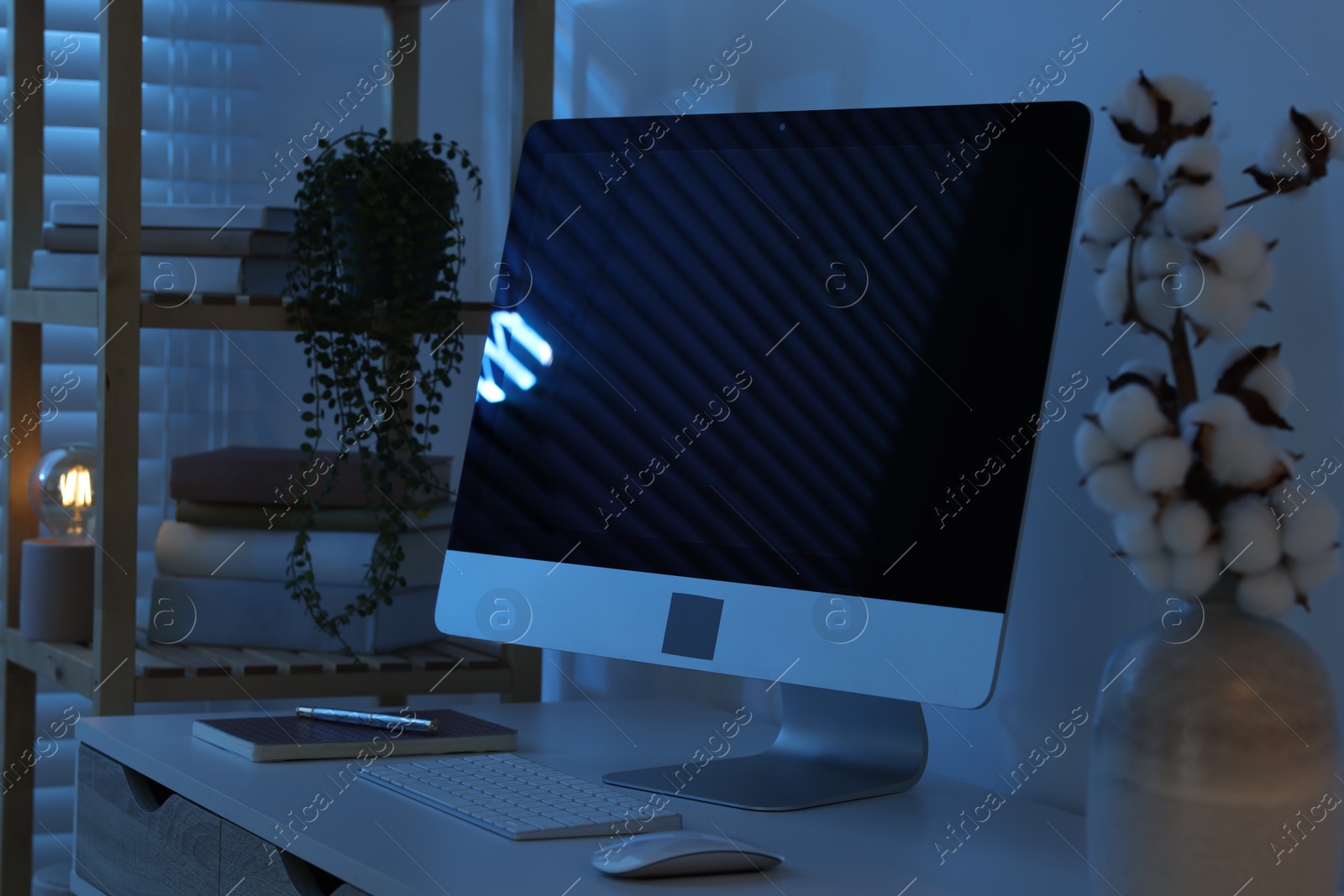 Comfortable workplace with computer on desk at home office in evening Photo of Comfortable workplace with computer on desk at home office in evening