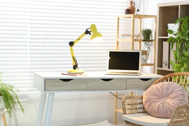 Photo of Home office. Comfortable workplace with laptop and lamp on desk indoors