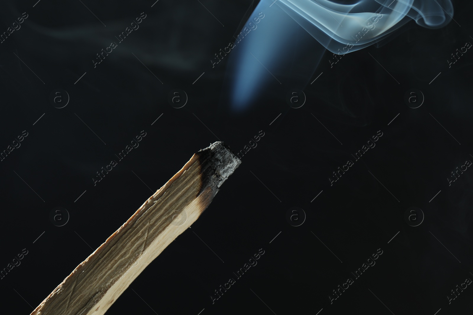 Photo of Smoldering palo santo stick against black background, closeup