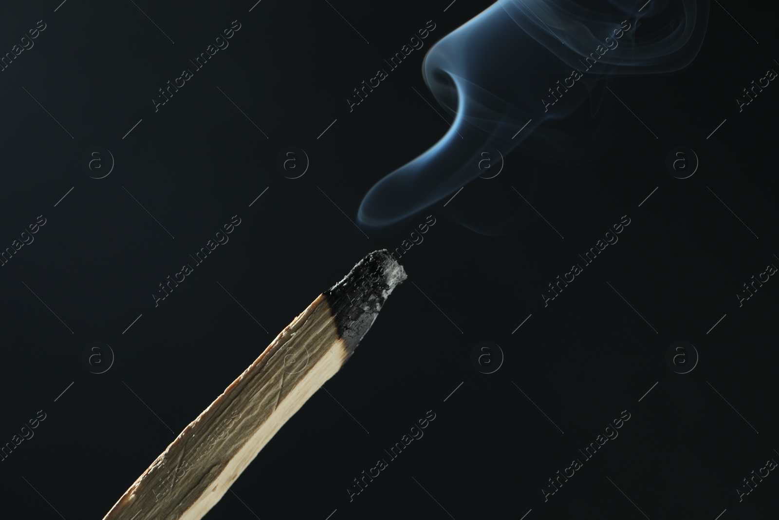 Photo of Smoldering palo santo stick against black background, closeup