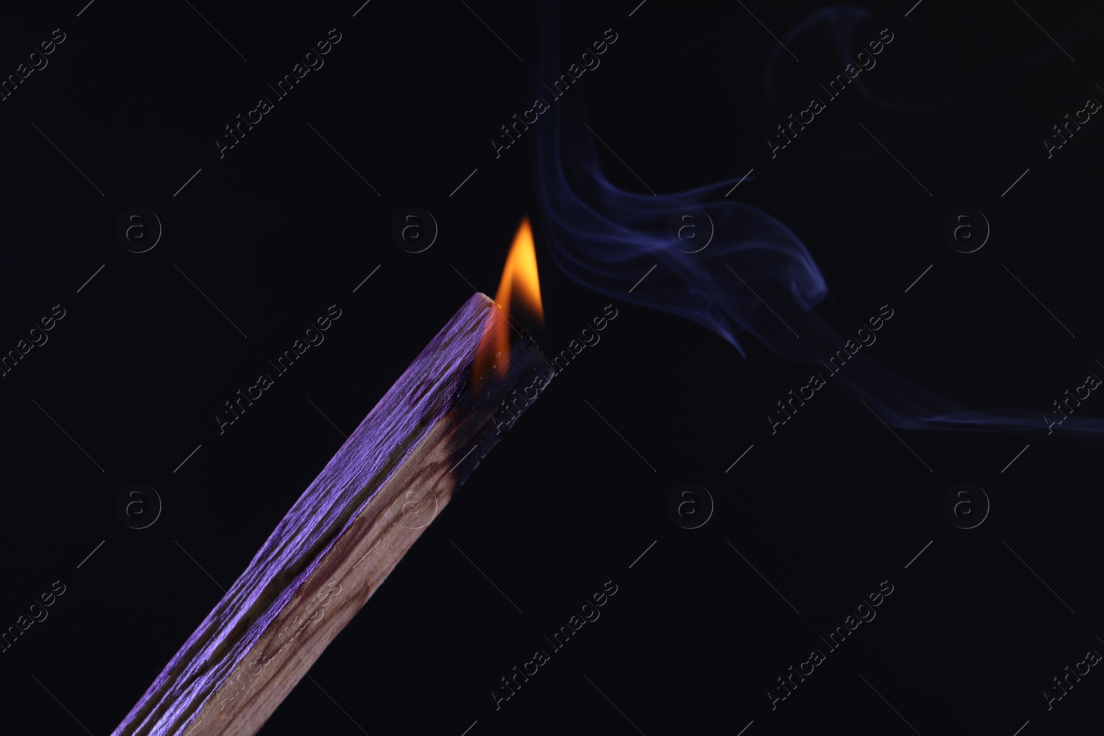 Photo of Burning palo santo stick against black background, closeup