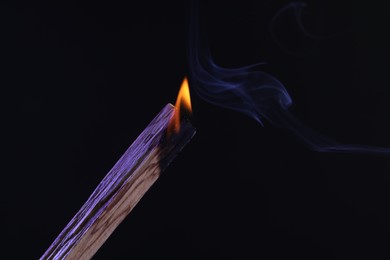 Photo of Burning palo santo stick against black background, closeup