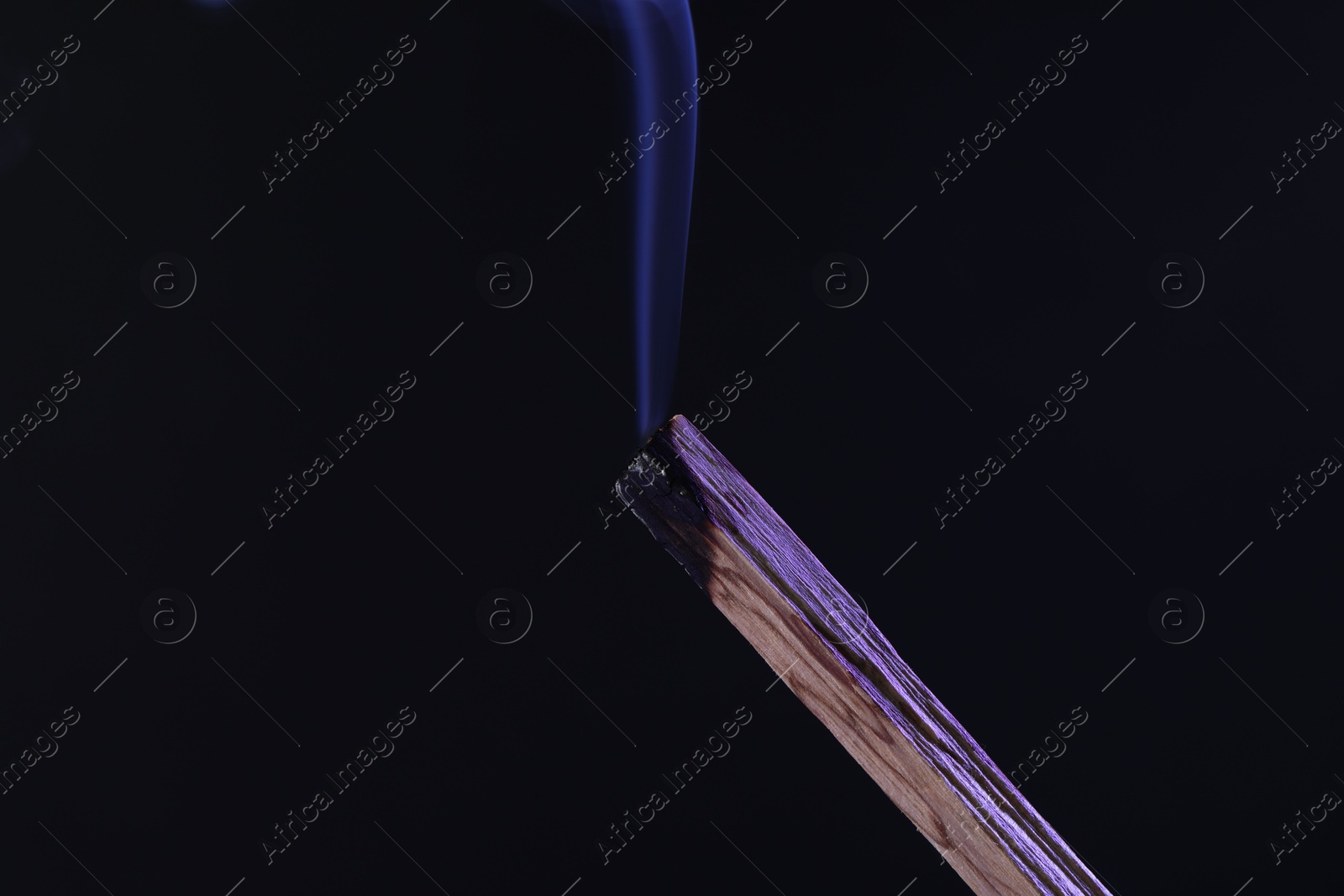 Photo of Smoldering palo santo stick against black background, closeup