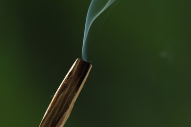 Photo of Smoldering palo santo stick against green background, closeup. Space for text