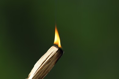 Photo of Burning palo santo stick against green background, closeup. Space for text