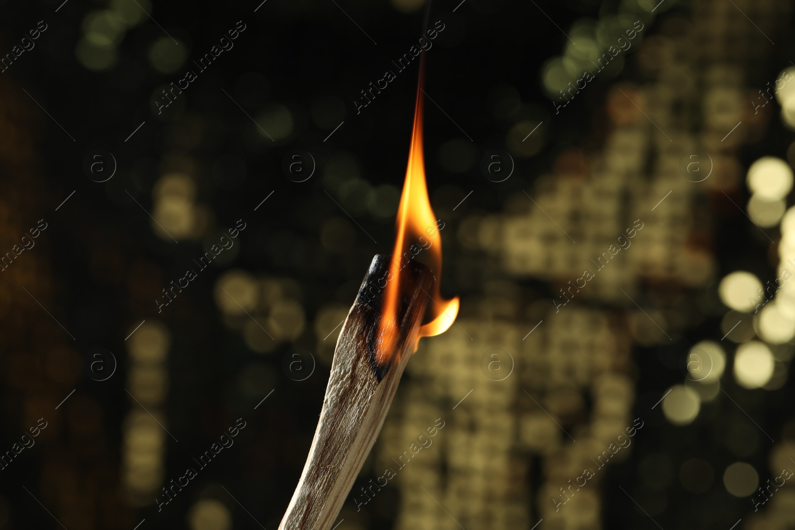 Photo of Burning palo santo stick against blurred background, closeup