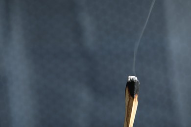 Photo of Smoldering palo santo stick against grey background, closeup. Space for text