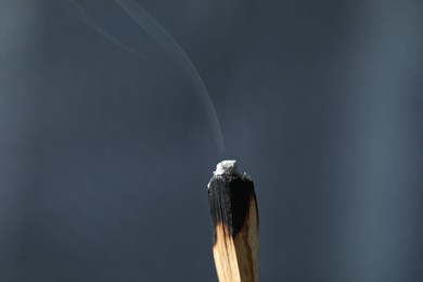 Photo of Smoldering palo santo stick against grey background, closeup