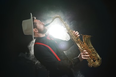 Photo of Professional musician playing saxophone on black background with smoke