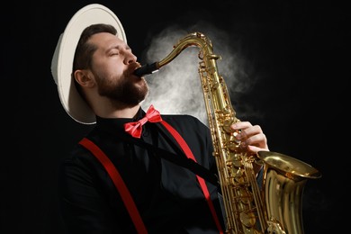 Photo of Professional musician playing saxophone on black background with smoke