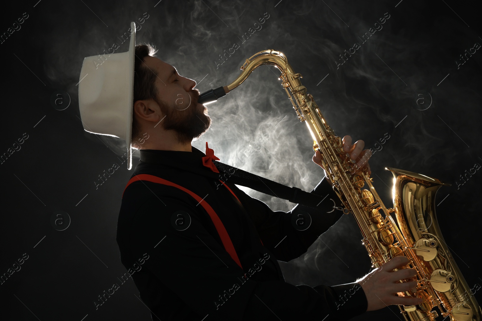 Photo of Professional musician playing saxophone on black background with smoke