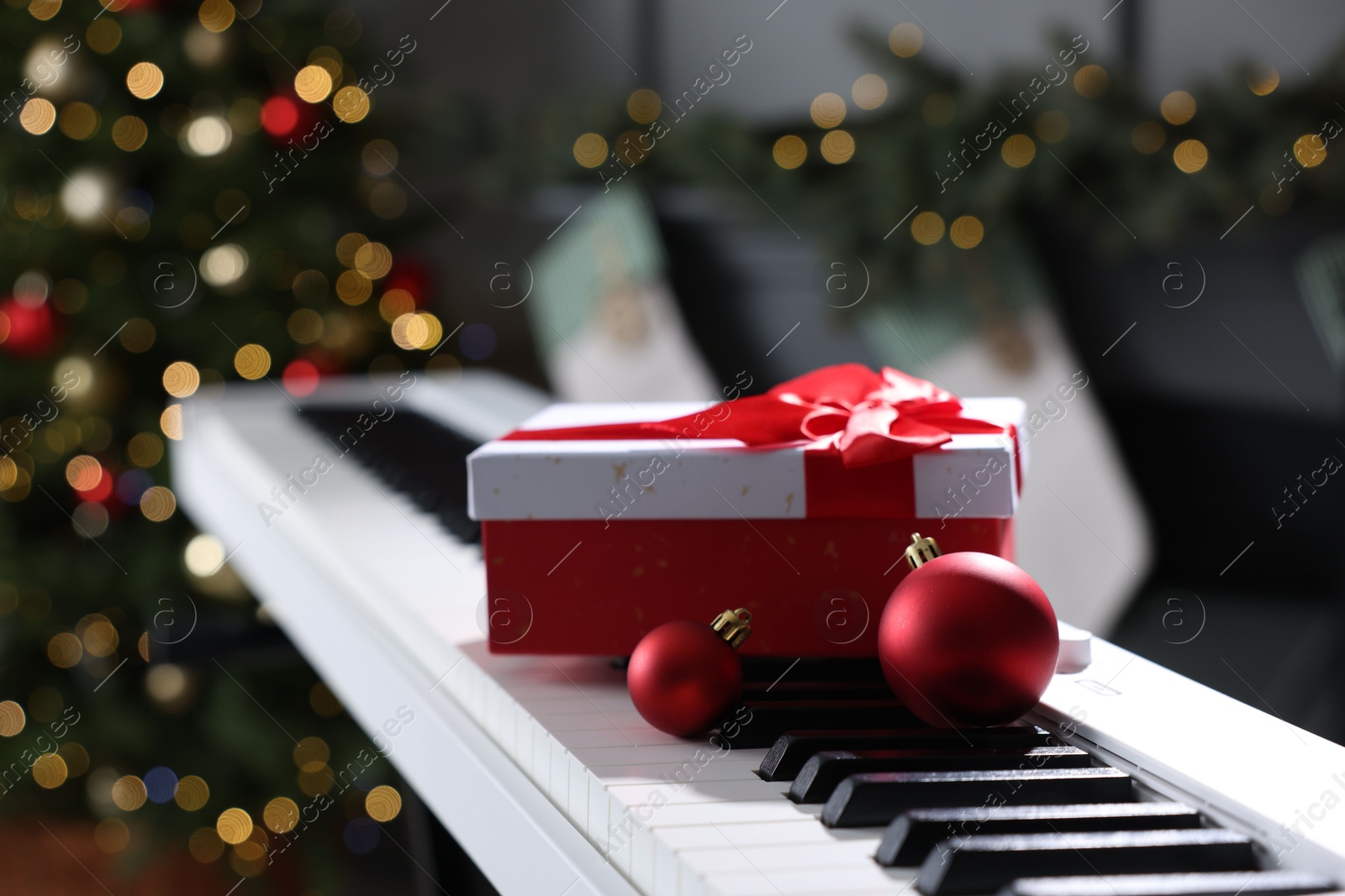 Gift and Christmas ornaments on piano against blurred lights, closeup. Bokeh effect Photo of Gift and Christmas ornaments on piano against blurred lights, closeup. Bokeh effect