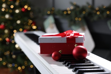 Photo of Gift and Christmas ornaments on piano against blurred lights, closeup. Bokeh effect