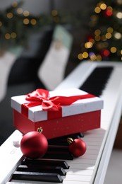 Photo of Gift and Christmas ornaments on piano against blurred lights, closeup. Bokeh effect