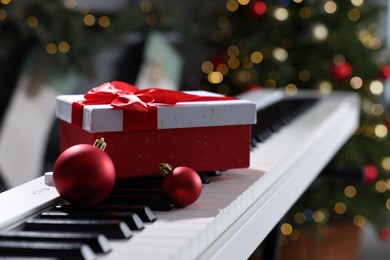 Photo of Gift and Christmas ornaments on piano against blurred lights, closeup. Bokeh effect