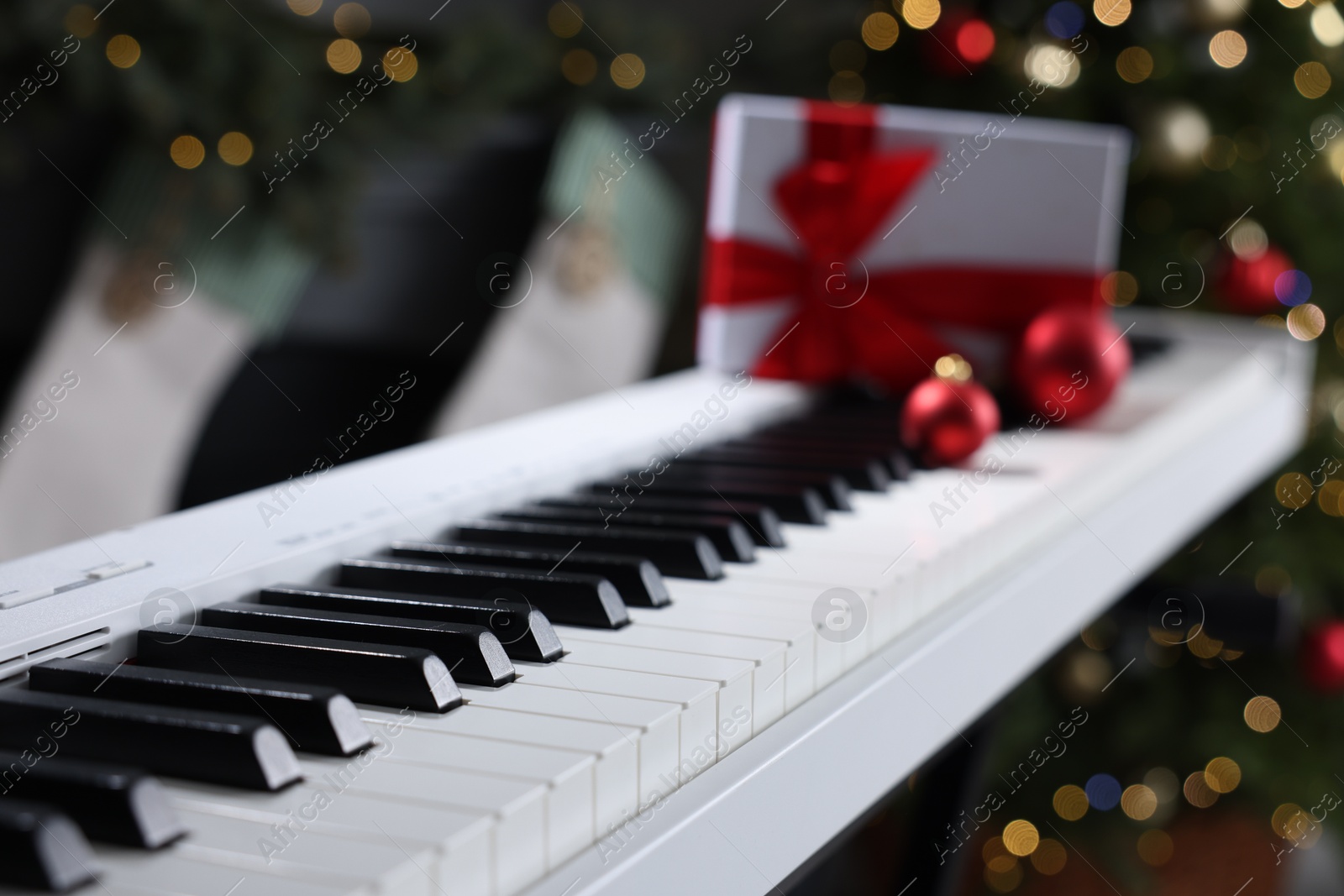 Gift and Christmas ornaments on piano against blurred lights, closeup. Bokeh effect Photo of Gift and Christmas ornaments on piano against blurred lights, closeup. Bokeh effect