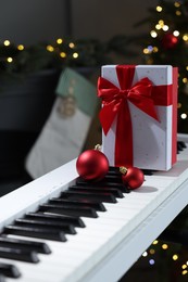 Gift and Christmas ornaments on piano against blurred lights, closeup. Bokeh effect