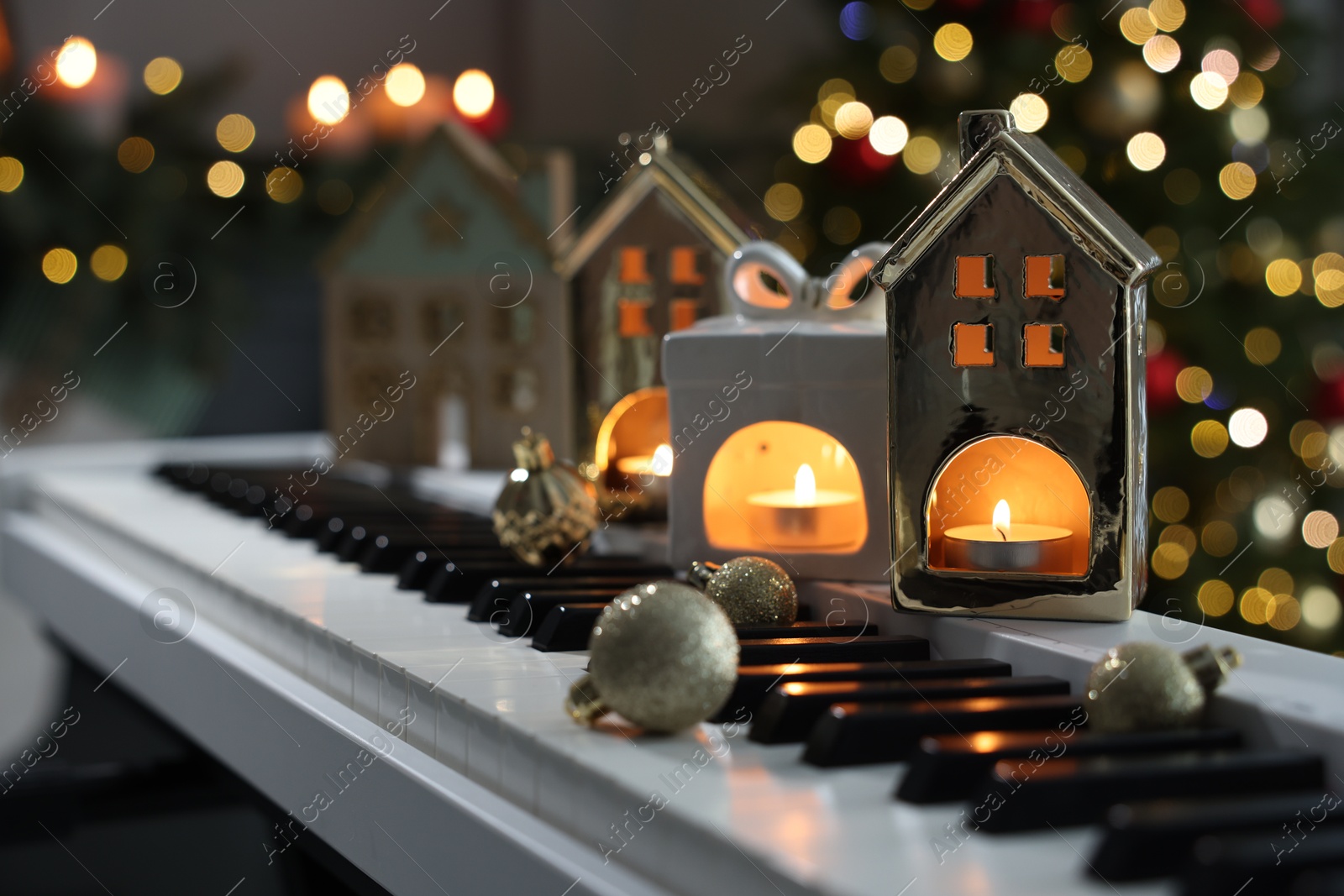 Christmas ornaments and house shaped holders with burning candles on electric piano against blurred lights, closeup. Bokeh effect Photo of Christmas ornaments and house shaped holders with burning candles on electric piano against blurred lights, closeup. Bokeh effect
