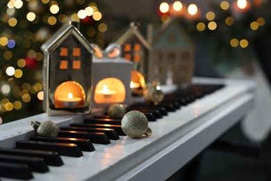 Christmas ornaments and house shaped holders with burning candles on electric piano against blurred lights, closeup. Bokeh effect