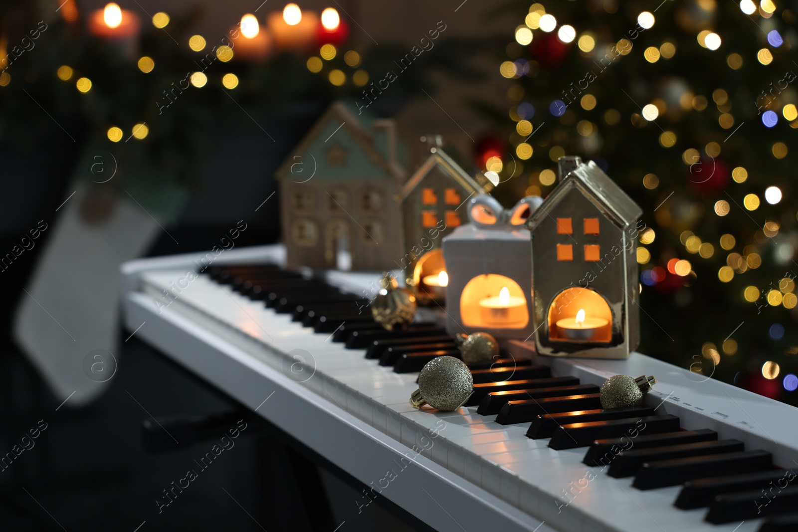 Christmas ornaments and house shaped holders with burning candles on electric piano against blurred lights, closeup. Bokeh effect Photo of Christmas ornaments and house shaped holders with burning candles on electric piano against blurred lights, closeup. Bokeh effect