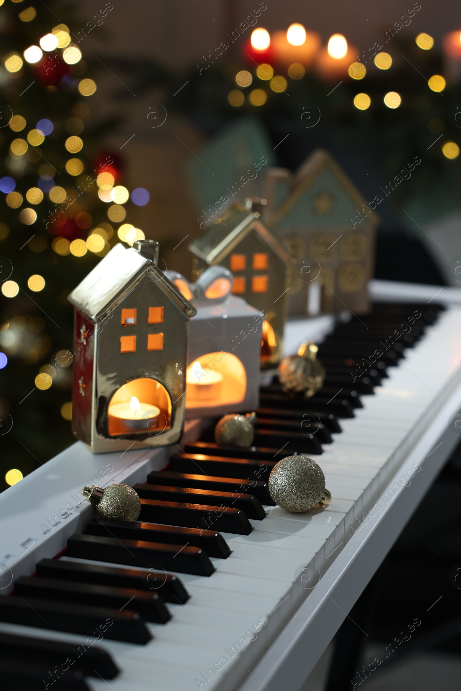 Christmas ornaments and house shaped holders with burning candles on electric piano against blurred lights, closeup. Bokeh effect Photo of Christmas ornaments and house shaped holders with burning candles on electric piano against blurred lights, closeup. Bokeh effect