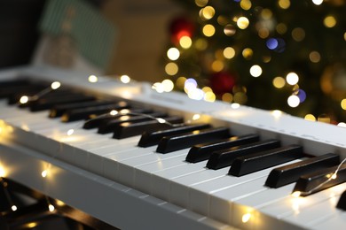 Photo of Electric piano against Christmas tree with blurred lights, closeup. Bokeh effect