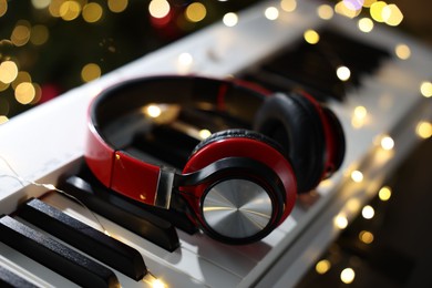 Photo of Headphones on electric piano against blurred lights, closeup. Bokeh effect