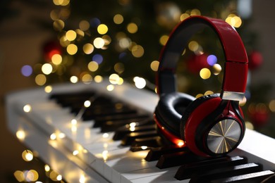 Photo of Headphones on electric piano against Christmas tree with blurred lights, closeup. Bokeh effect