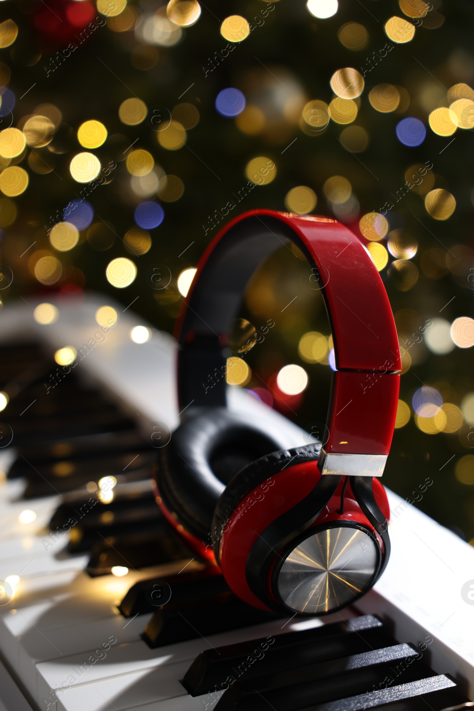 Photo of Headphones on electric piano against Christmas tree with blurred lights, closeup. Bokeh effect